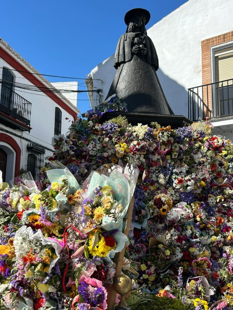 Así se encuentra el monumento de la Virgen del Rocío de Pastora. Lleno de flores por los diversos centros educativos 